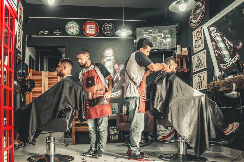 A bustling barbershop with two men getting haircuts, showcasing a vibrant barber environment. For use in small business website price page