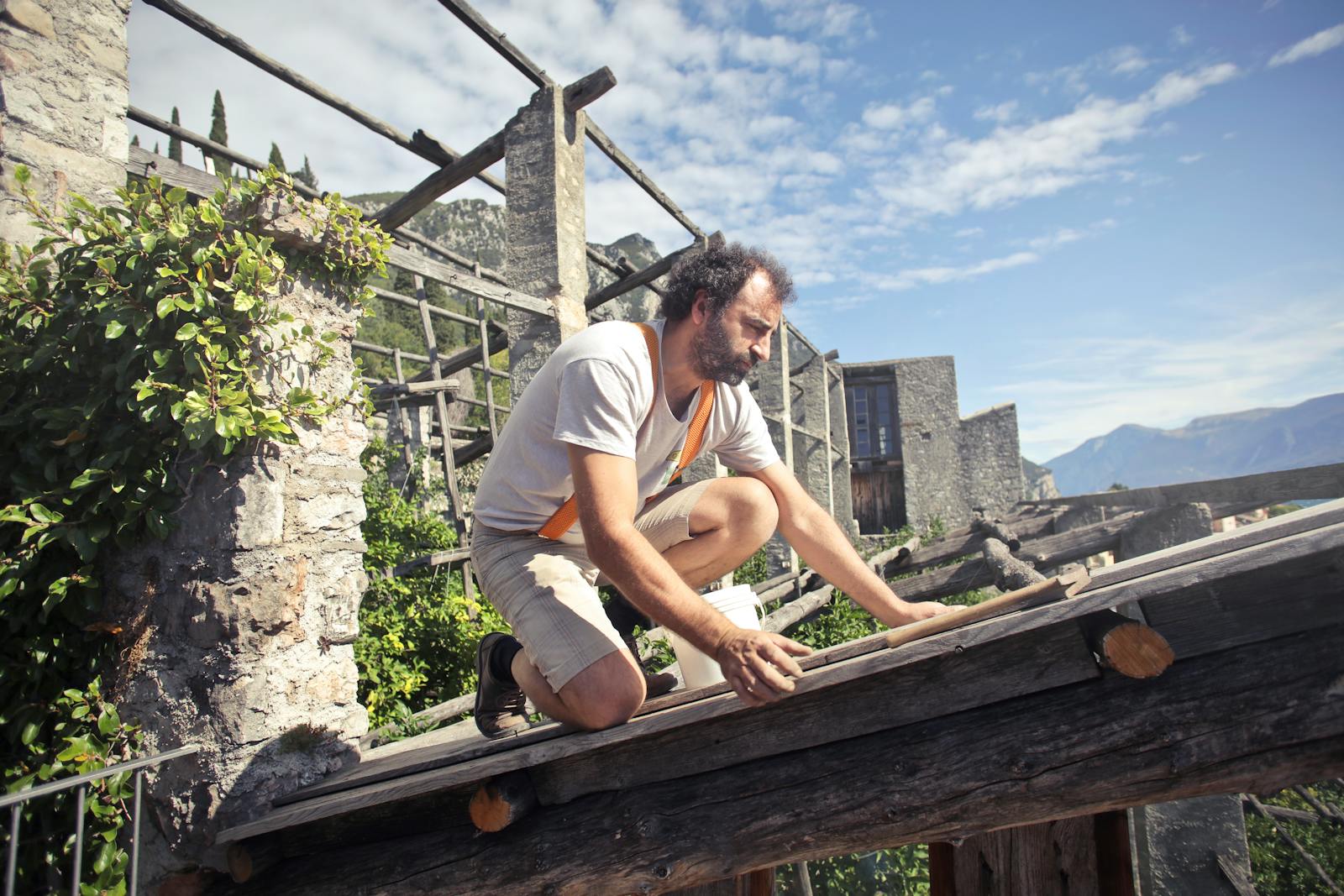 A man kneeling on a rooftop under construction in a picturesque mountainous landscape on a sunny day for use in small business website price page