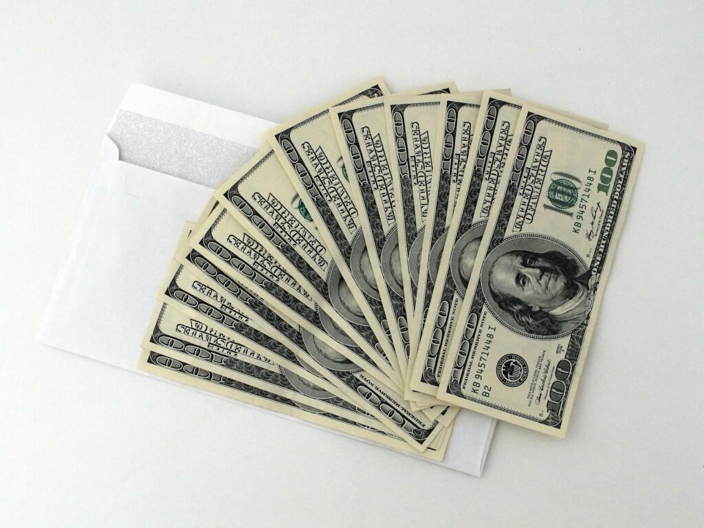 Fan of US $100 bills partially out of a white envelope on a white background header image for how to get sba microloan for website upgrade post