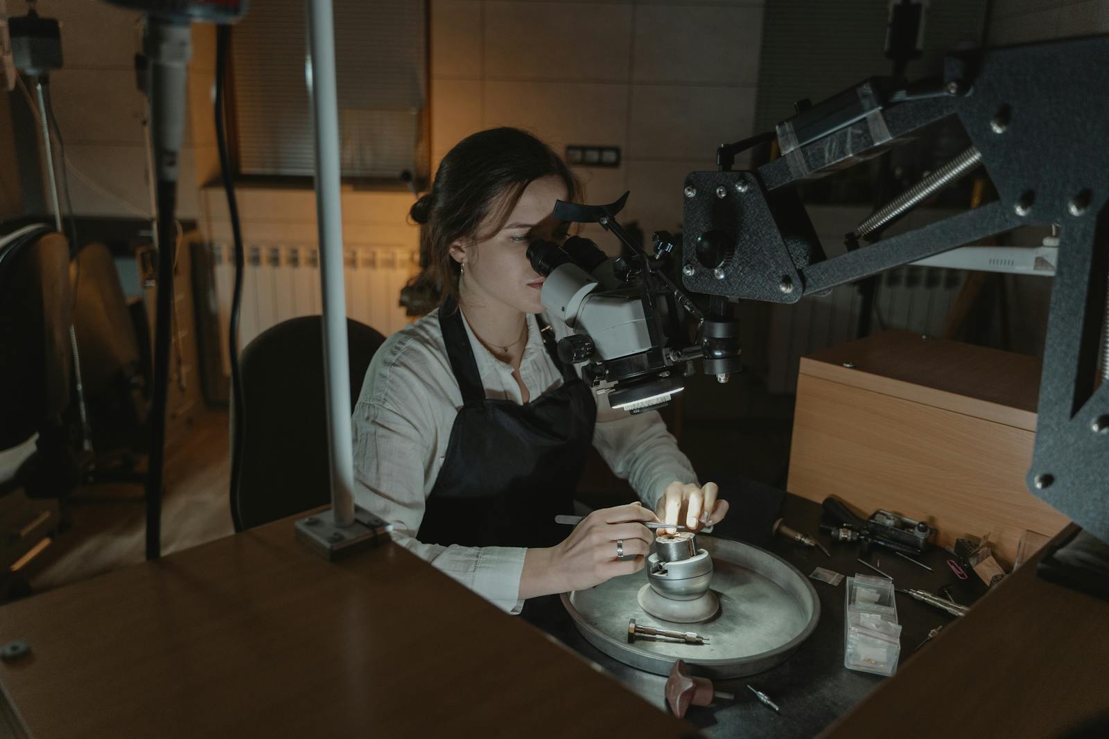 A woman jeweler crafting intricate pieces with precision under a microscope in a workshop for use in small business website price page